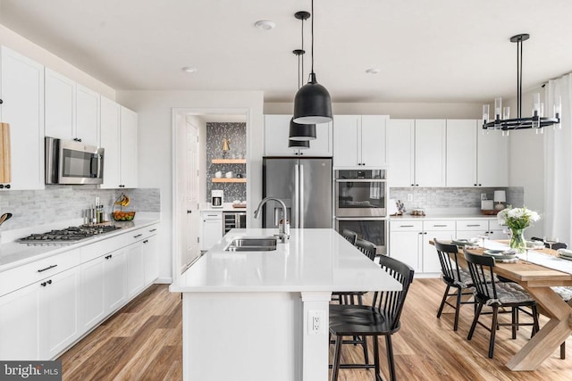 kitchen featuring a sink, stainless steel appliances, tasteful backsplash, light wood finished floors, and white cabinetry