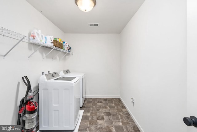 clothes washing area featuring separate washer and dryer, stone finish floors, and baseboards