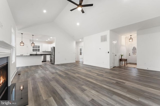 unfurnished living room featuring a ceiling fan, high vaulted ceiling, a warm lit fireplace, dark wood-type flooring, and recessed lighting