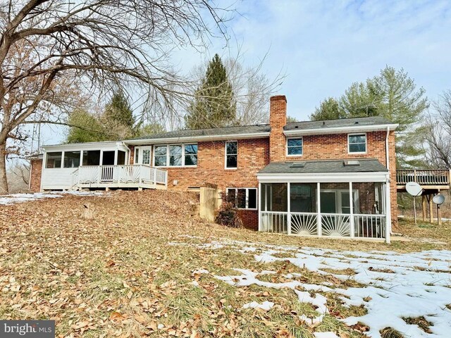 snow covered back of property with a wooden deck and a sunroom