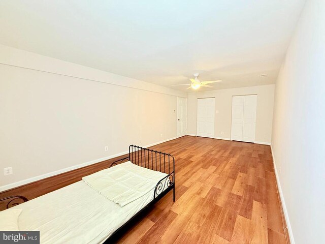 bedroom featuring two closets, light hardwood / wood-style flooring, and ceiling fan