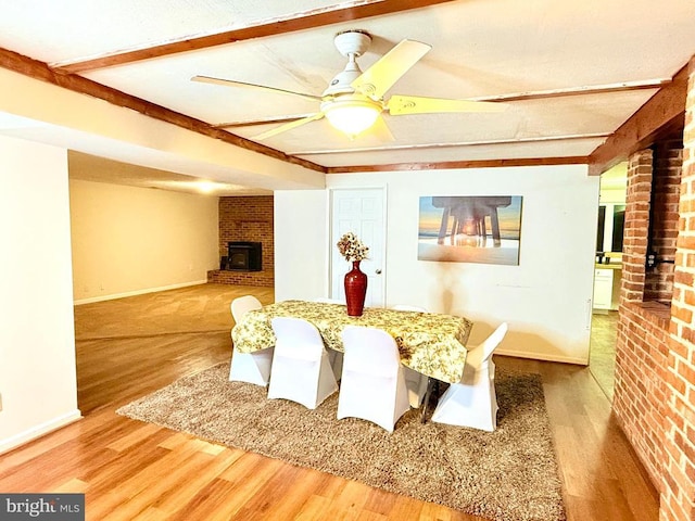 dining area featuring beam ceiling, ceiling fan, brick wall, a fireplace, and hardwood / wood-style floors