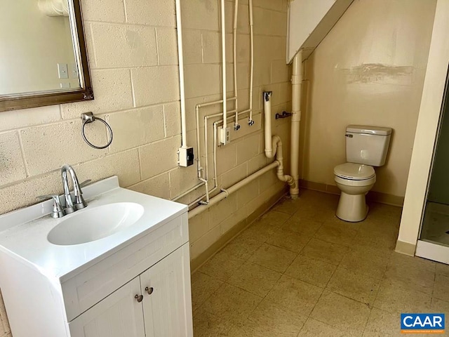 bathroom with toilet, walk in shower, vanity, and concrete block wall