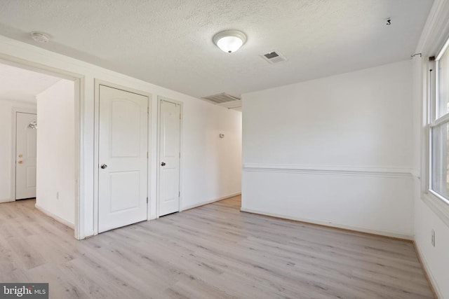 unfurnished bedroom with light wood-type flooring, visible vents, baseboards, and a textured ceiling