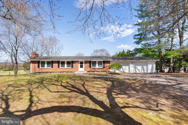 single story home featuring a chimney, driveway, brick siding, and an attached garage