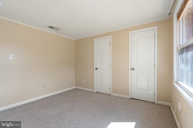 unfurnished bedroom with baseboards, ornamental molding, visible vents, and carpet
