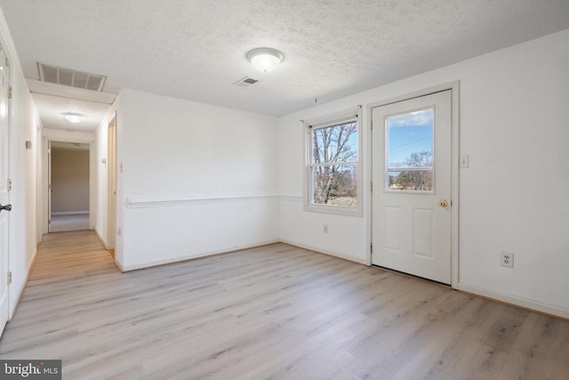 empty room featuring a textured ceiling, visible vents, light wood-style flooring, and baseboards