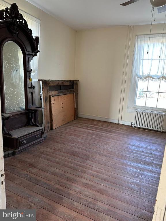 unfurnished living room with a ceiling fan, baseboards, radiator, crown molding, and hardwood / wood-style floors