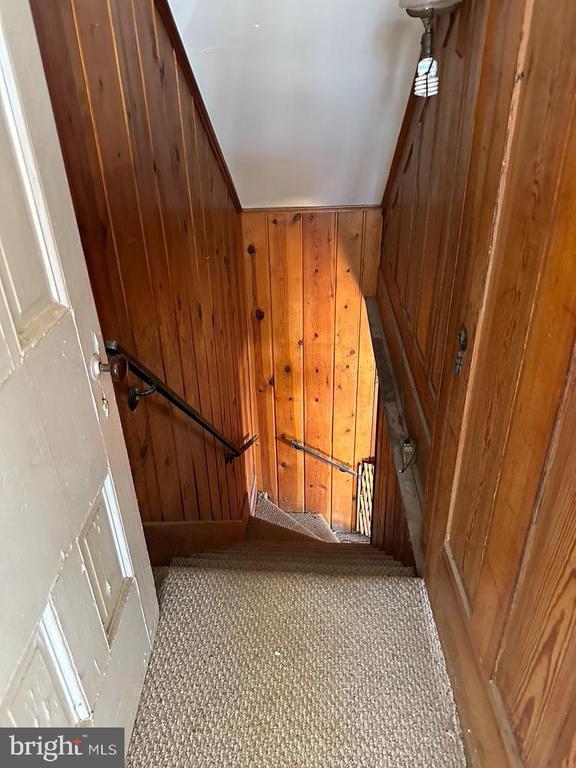 stairway featuring lofted ceiling, carpet flooring, and wood walls