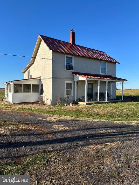 rear view of house with metal roof, a sunroom, stucco siding, and a chimney