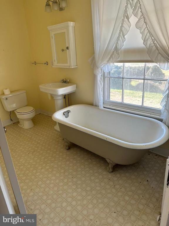 full bath with tile patterned floors, toilet, a freestanding tub, and a sink