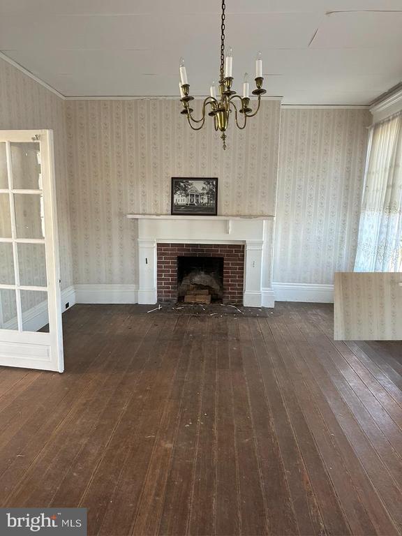 unfurnished living room featuring crown molding, dark wood finished floors, a brick fireplace, and a notable chandelier