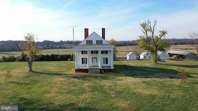 rear view of house with covered porch, a chimney, and a lawn