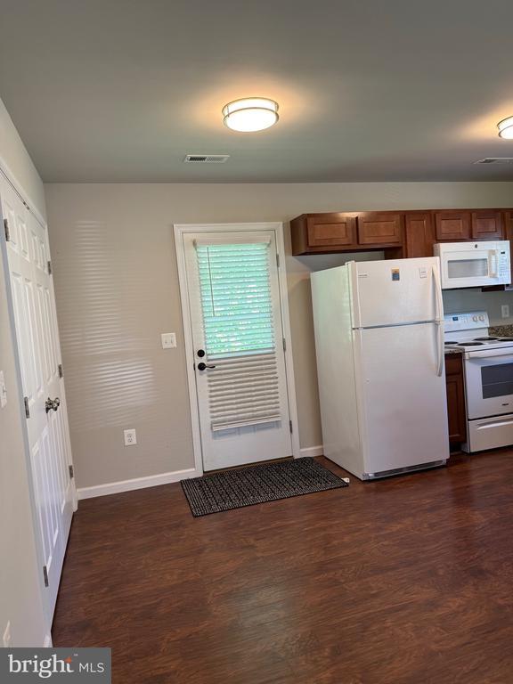 kitchen featuring white appliances, brown cabinets, dark wood-style floors, and baseboards