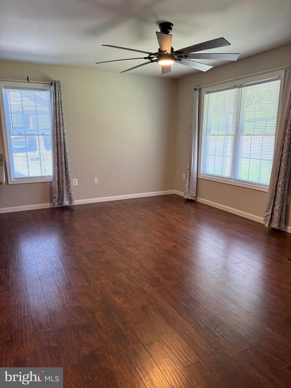 unfurnished room with dark wood-type flooring, healthy amount of natural light, ceiling fan, and baseboards