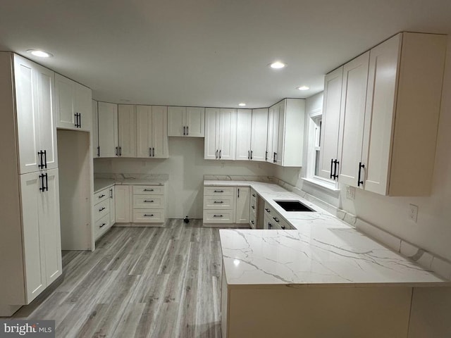 kitchen featuring light stone countertops, light wood finished floors, recessed lighting, white cabinetry, and a peninsula