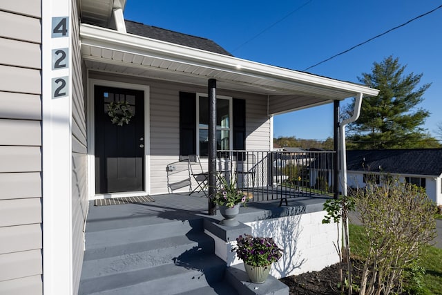entrance to property featuring covered porch and a shingled roof