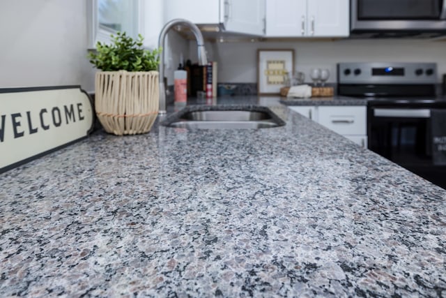 kitchen with light stone countertops, a sink, stainless steel microwave, white cabinets, and range with electric stovetop