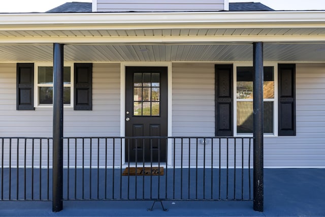 doorway to property featuring a porch and roof with shingles