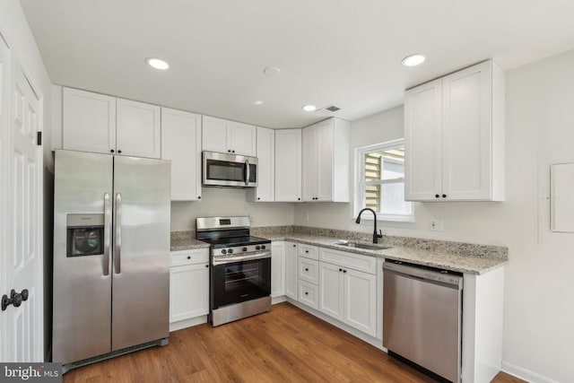 kitchen with appliances with stainless steel finishes, a sink, white cabinetry, light stone counters, and recessed lighting