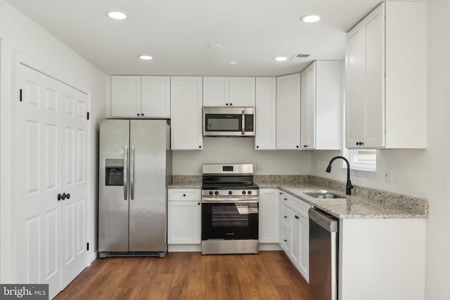 kitchen featuring appliances with stainless steel finishes, a sink, white cabinets, wood finished floors, and light stone counters
