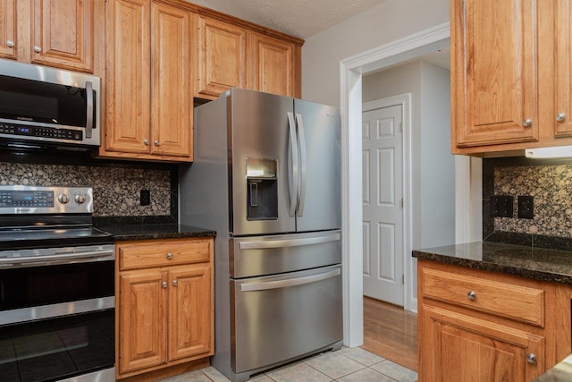 kitchen with light tile patterned flooring, tasteful backsplash, a textured ceiling, dark stone countertops, and stainless steel appliances