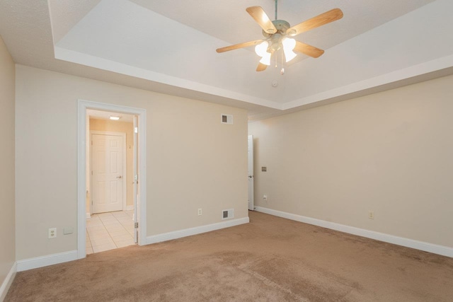 unfurnished room with ceiling fan, a tray ceiling, and light carpet