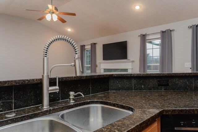 kitchen with lofted ceiling, sink, dark stone counters, and ceiling fan