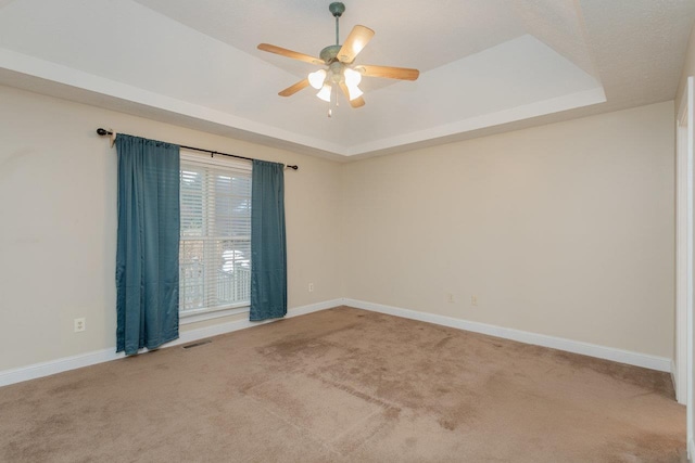 carpeted empty room with ceiling fan and a raised ceiling