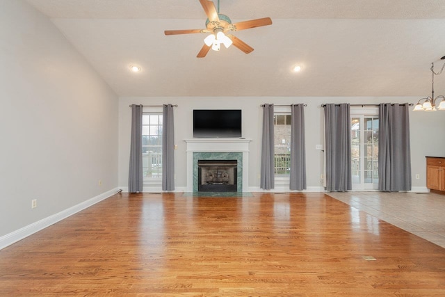 unfurnished living room with a high end fireplace, vaulted ceiling, light hardwood / wood-style floors, and ceiling fan with notable chandelier