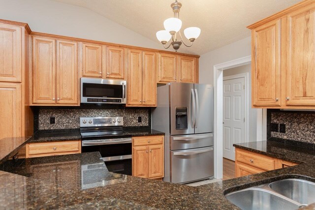 kitchen with vaulted ceiling, hanging light fixtures, dark stone countertops, appliances with stainless steel finishes, and decorative backsplash