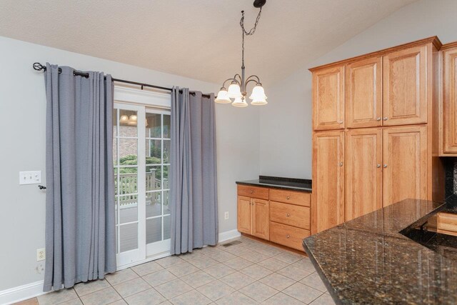 kitchen with vaulted ceiling, dark stone countertops, hanging light fixtures, light tile patterned floors, and a notable chandelier