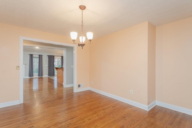 empty room featuring wood-type flooring, a textured ceiling, and a notable chandelier