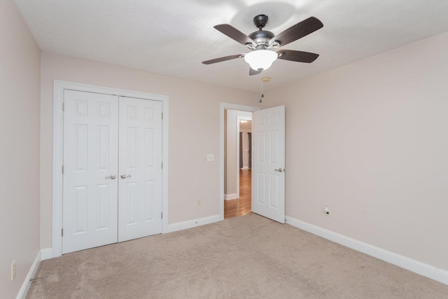 unfurnished bedroom with ceiling fan, light colored carpet, a closet, and a textured ceiling