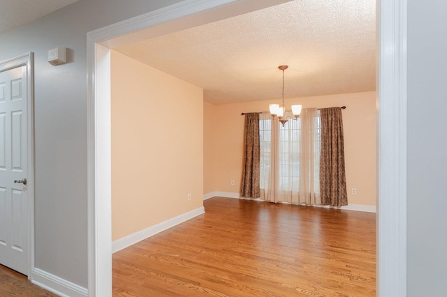 empty room featuring an inviting chandelier, hardwood / wood-style floors, and a textured ceiling