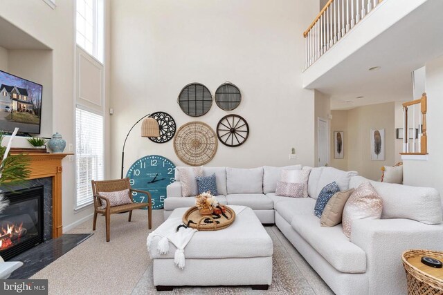 carpeted living area with a towering ceiling, healthy amount of natural light, and a premium fireplace