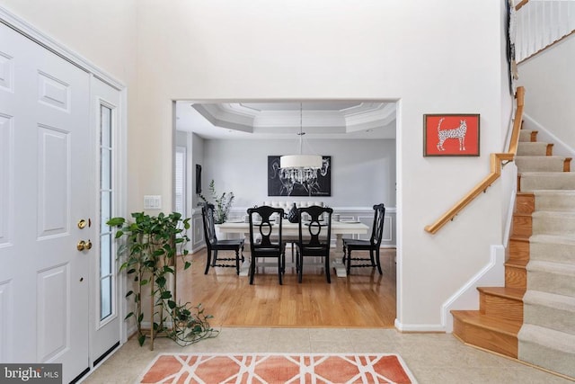 entryway featuring stairway, crown molding, tile patterned floors, a raised ceiling, and baseboards