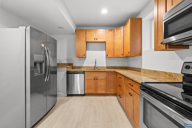 kitchen featuring light wood-style flooring, a sink, appliances with stainless steel finishes, light stone counters, and recessed lighting
