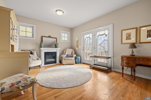 living area featuring baseboards, light wood-type flooring, and a glass covered fireplace