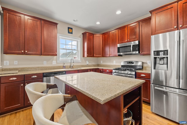 kitchen featuring light stone countertops, a sink, a kitchen island, reddish brown cabinets, and stainless steel appliances