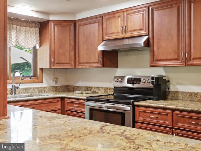  - kitchen featuring stainless steel range with electric cooktop, under cabinet range hood, and brown cabinets