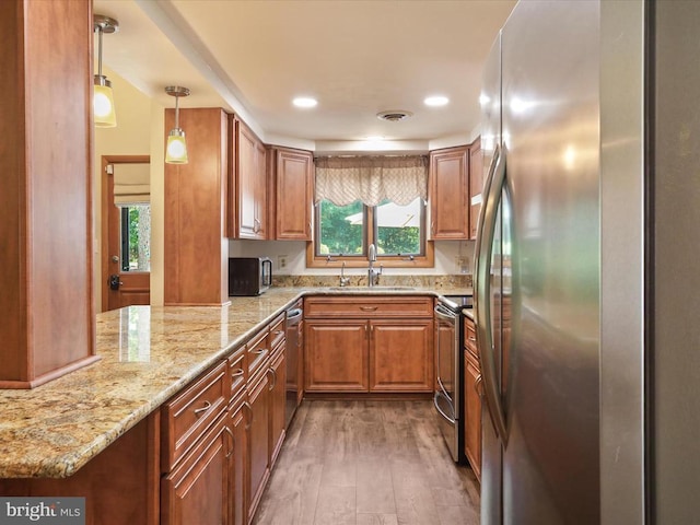  - kitchen featuring stainless steel appliances, wood finished floors, brown cabinetry, light stone counters, and pendant lighting