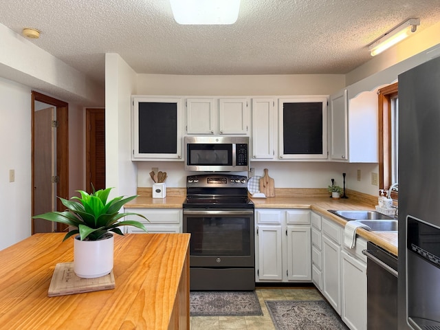 kitchen featuring appliances with stainless steel finishes, a textured ceiling, white cabinets, a sink, and wooden counters