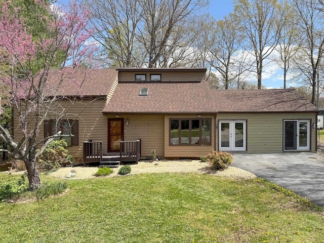 rear view of property featuring driveway, roof with shingles, a yard, and a wooden deck