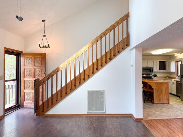 foyer with light wood-style flooring, a chandelier, high vaulted ceiling, stairs, and baseboards