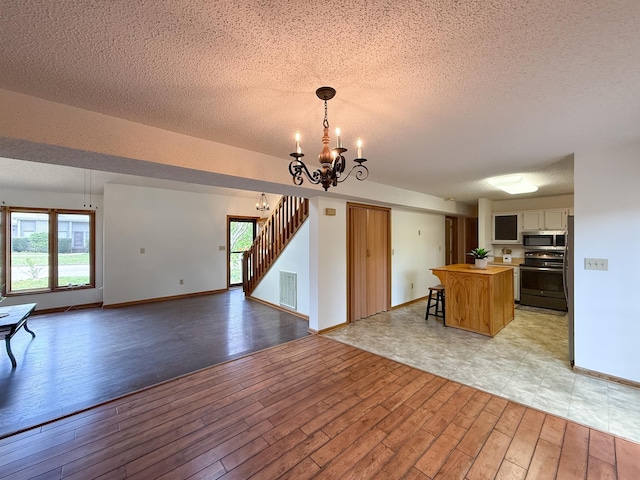 kitchen with electric range oven, stainless steel microwave, open floor plan, a textured ceiling, and light wood-style floors