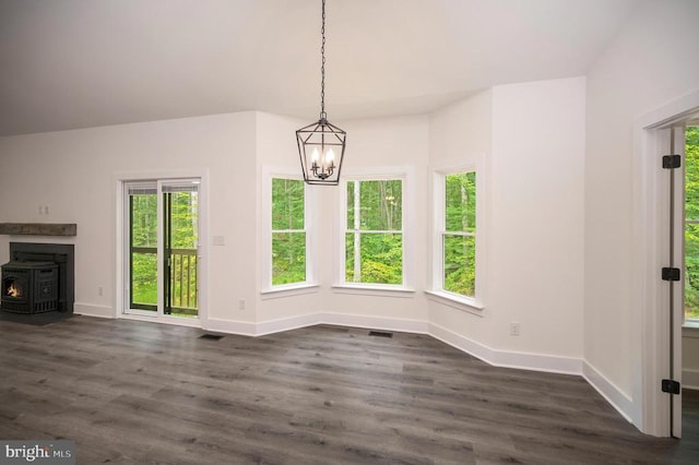  - unfurnished dining area featuring a chandelier, a wood stove, and dark wood-style flooring
