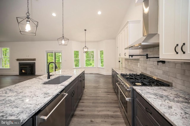  - kitchen with appliances with stainless steel finishes, wall chimney exhaust hood, white cabinets, backsplash, and light stone counters