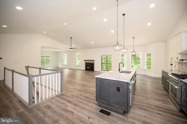  - kitchen featuring stainless steel stove, vaulted ceiling, light stone counters, a kitchen island with sink, and white cabinets