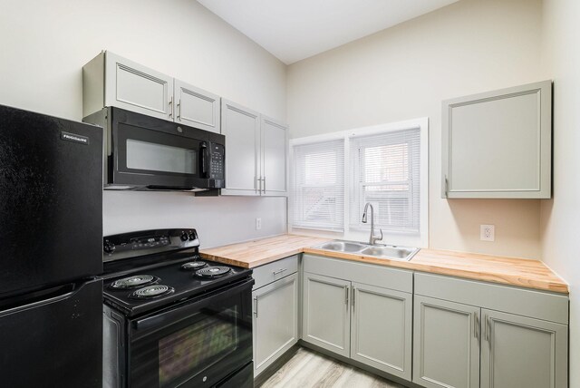 kitchen featuring butcher block counters, sink, gray cabinetry, black appliances, and light wood-type flooring